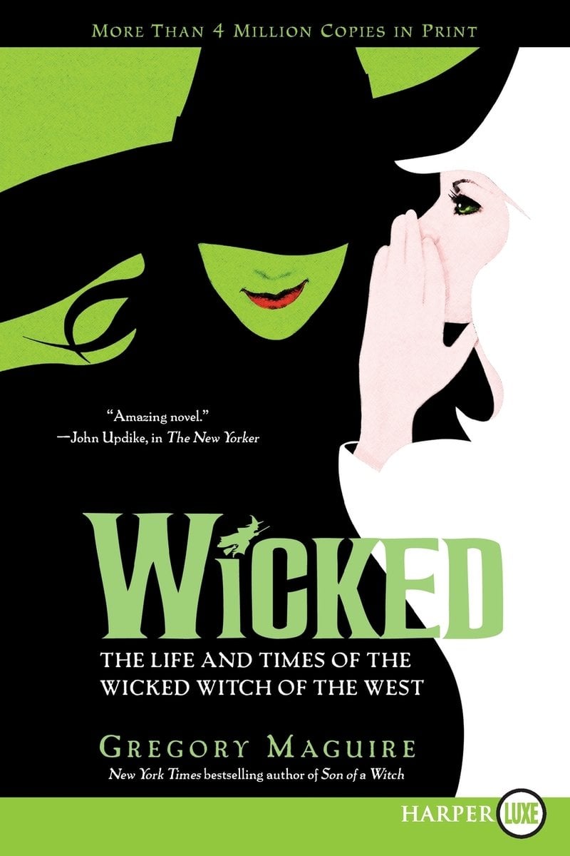 Wicked: The Life and Times of the Wicked Witch of the West by Gregory Maguire. A woman all in white whispers something into the ear of another woman, this one with a green face and her head tilted down so her large black hat covers her eyes.