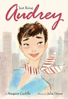 Just Being Audrey by Margaret Cardillo and illustrated by Julia Denos, a children's book cover. An illustration of Audrey Hepburn with a short bob, rosy cheeks, and a smile on her face is front and center. She wears a red and white striped ascot and a collared blue dress. Behind her are illustrations of buildings, resembling a big city.