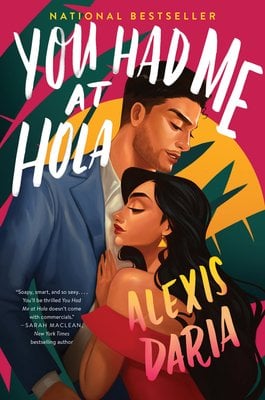 Cover of You Had Me at Hola by Alexis Daria. A woman in a pink dress is leaning against the chest of a man with a blue blazer. The background consist of green palms, a yellow sun, and a pink sky.
