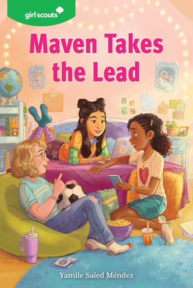 Girl Scouts: Maven Takes the Lead by Yamile Saied Méndez shows three girls in a brightly lit bedroom. One girl is laying sitting up on her bed with a computer, another is sitting on the floor with a notebook, and the third is sitting on a green beanbag with a soccer ball in her lap.