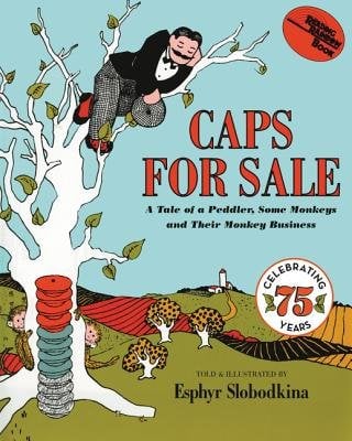 Caps For Sale by Esphyr Slobodkina features a man in a black blazer and checkered pants sleeping on a branch in a tree. A stack of caps are neatly placed at the base of the tree with two monkeys peering out behind the trunk. The background features a solid blue sky and rolling hills used for farmland. A silo can be seen on a far hill in the very back.