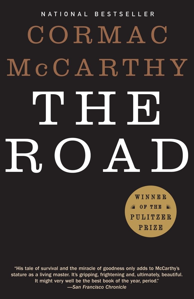 The Road by Cormac McCarthy, a literary fiction book cover. An all black cover with "THE ROAD" written in a white, capitalized font in the center of the cover with "CORMAC McCARTHY" written above it, slightly smaller, in a faded orange.