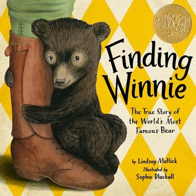Book cover of Finding Winnie: The True Story of the World's Most Famous Bear by Lindsay Mattick, Illustrated by Sophie Blackall, featuring a small dark brown bear cub sitting with his forepaws curled around a leg wearing a tall leather boot against a yellow and white diamond background.