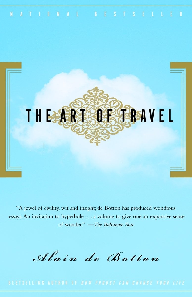 The Art of Travel by Alain de Botton, a travel guide book cover depicting a black title on an ornate gold etching boxed in by two gold strips. It is on a blue background with a single cloud. The author's name is also in black, with a quote praising the book above it.