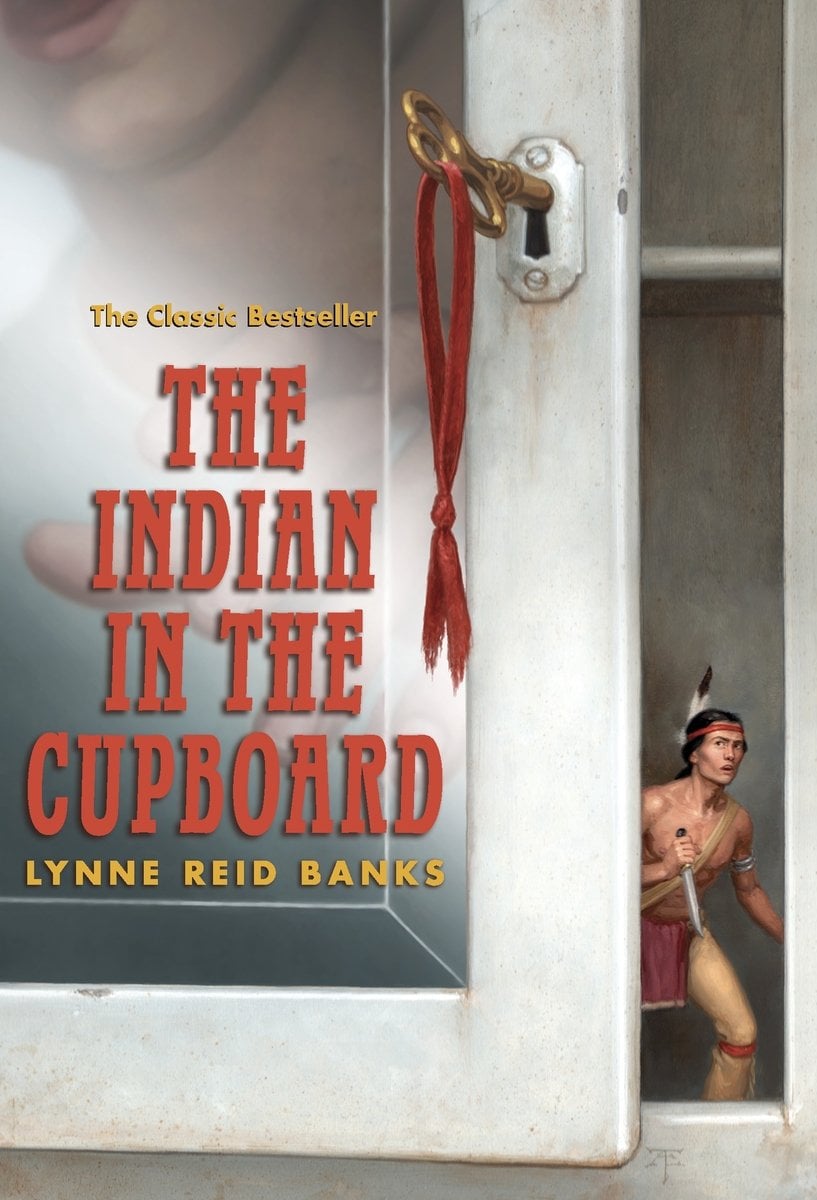 The Indian in the Cupboard by Lynne Reid Banks's book cover depicts a slightly ajar cupboard door that has a young boy opening it with a key in the reflection. In the cupboard is a small doll-sized American Indian man peaking out with a knife.