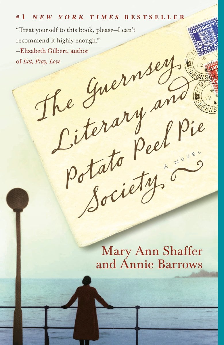The book cover for The Guernsey Literary and Potato Peel Pie Society by Mary Ann Shaffer and Annie Barrows. The silhouette of a woman leaning against a railing and looking out over a body of water toward an island in the distance. The title is written in brown cursive text on a yellowed envelope featuring blue and red postage stamps.