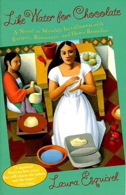 Book jacket of Like Water for Chocolate by Laura Esquivel. A woman in a long white dress with a red flower in her hair prepares food in her hands in a colorfully tiled kitchen. Behind her is a table with ingredients, including a red pepper and bowl. Another woman sits with an ingredients basket, wearing a white and green dress with a red shawl.