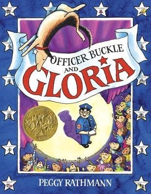 Officer Buckle and Gloria by Peggy Rathmann, book cover. A police officer is on stage holding white papers in front of a crowd of children, and everyone is gazing up as a dog does a flip in the air. The borders of this book are blue and have stars all around, with a white banner in the middle to display the title.