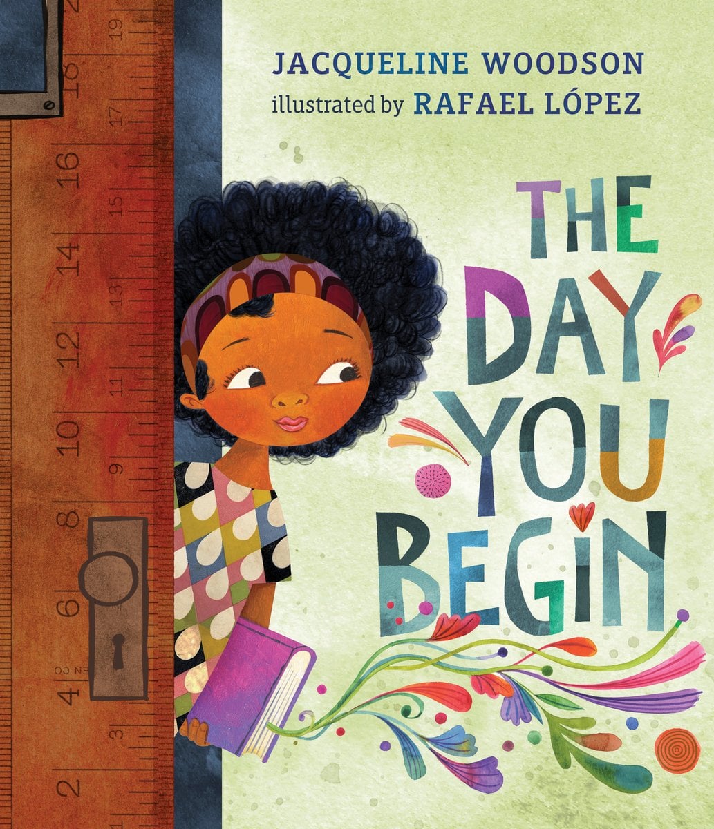 The Day You Begin by Jacqueline Woodson book cover features a girl holding a purple and pink book, poking out behind a solid oak door. The wall behind her is a lime-green color with the title written in bold, colorful fonts. The author's name appears at the very top in simple, blue font.