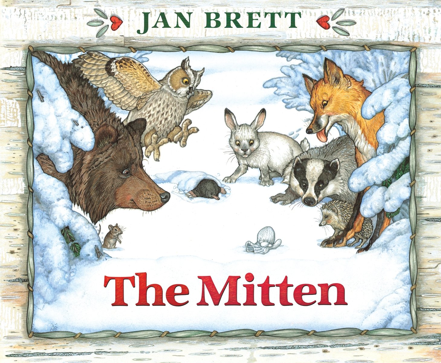 The Mitten by Jan Brett book cover features a snowy landscape as a group of forest animals -- owl, rabbit, raccoon, fox, hedgehog, and a bear gather around a single mitten. A white, wooden border goes around the cover with the title in bright red text center-bottom and the author's name at the very top in dark green.