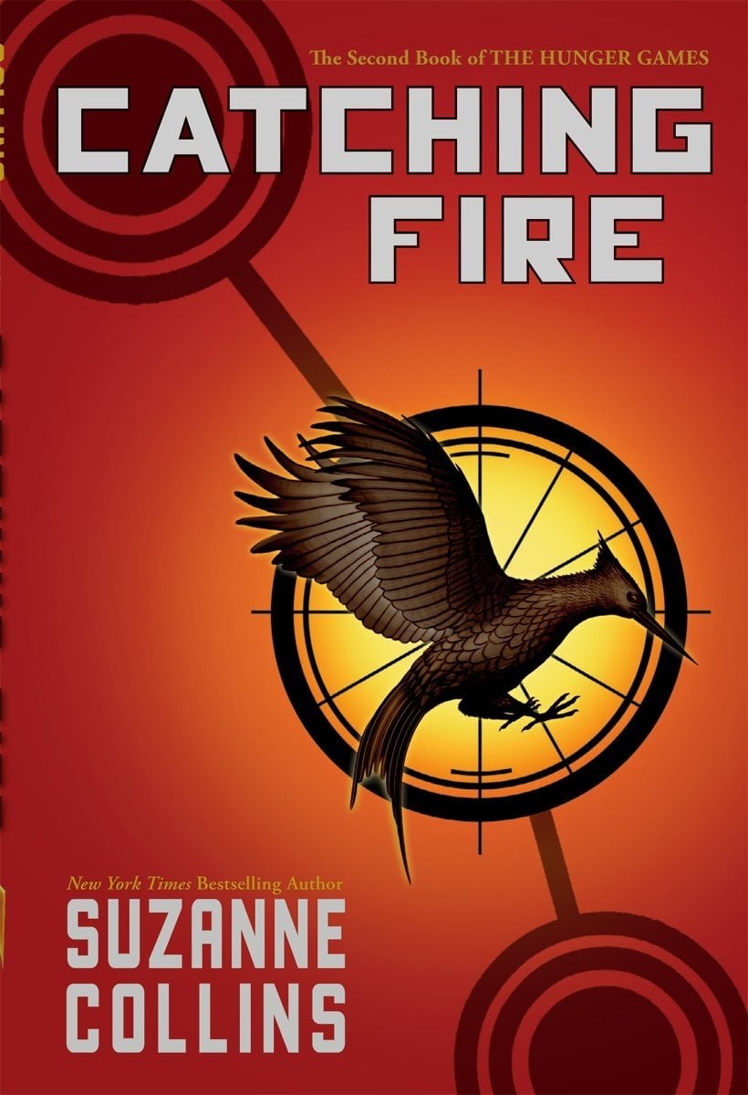 Book cover of Catching Fire by Suzanne Collins. Set on a fiery red background, a brown bird is encased in a black circle and haloed by a yellow light. The title and author name are in white.