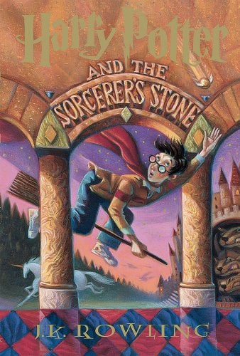 The book cover of Harry Potter and the Sorcerer's Stone. It depicts a boy with black hair and glasses flying under a stone archway on a broomstick. There is a unicorn and a castle behind him.