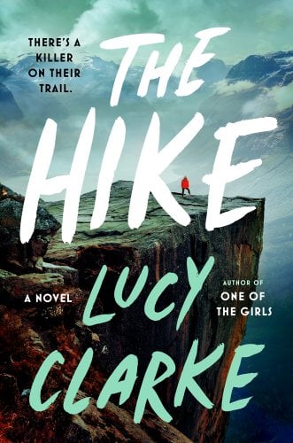 The Hike by Lucy Clarke book cover. A large cliff with a person in a red jacket standing near the edge.