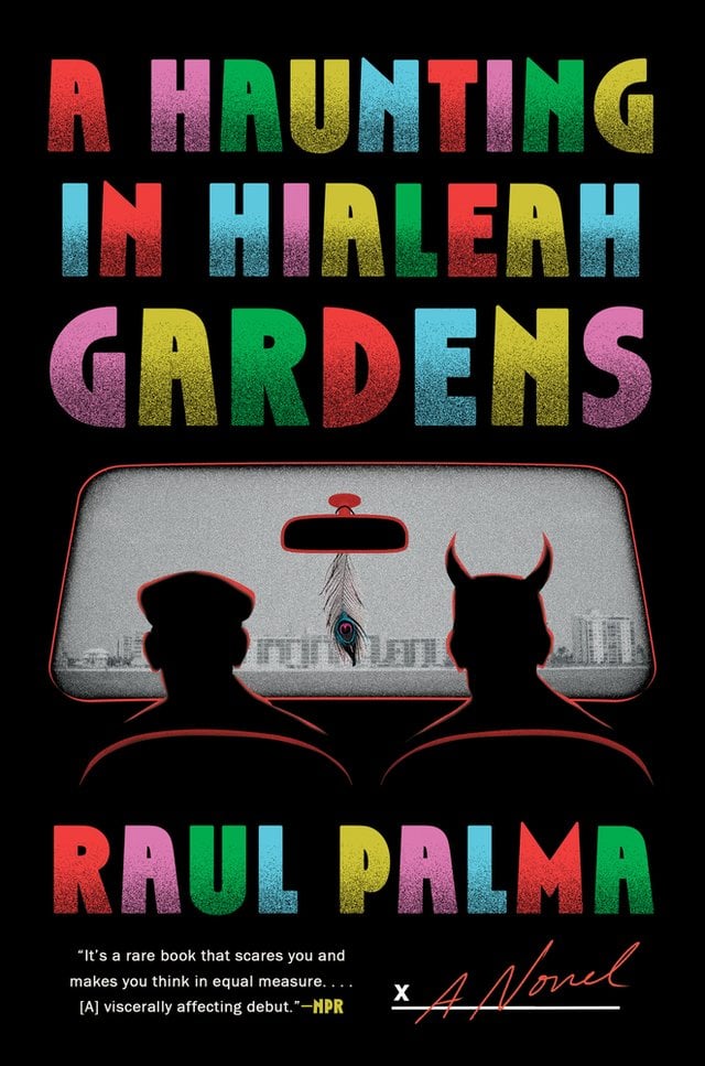 Two figures are sitting in the front seat of a vehicle. One is wearing a cap, while the other has horns. They look out to a beach lined with condos. A feather hangs from the rearview mirror.