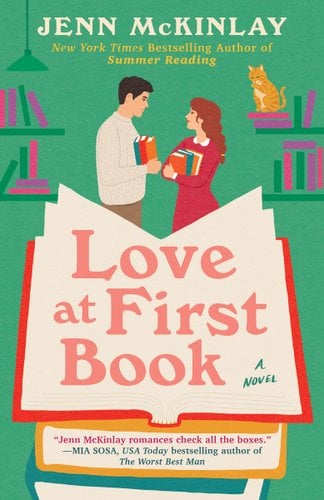 Book jacket of Love at First Book by Jenn McKinlay. In a library, a man in a beige sweater and brown pants looks at a woman with a red dress with a white collar. Both are holding books. A giant book with the title in the pages sits in front of them.
