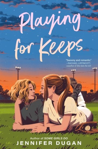 Two teenage girls lay together on an athletic field. On the right is a girl with short, curly blonde hair, grey shirt, and gold necklace. On the left is a girl with straight red hair, in a ponytail. She's wearing a baseball uniform. The sun sets behind them.