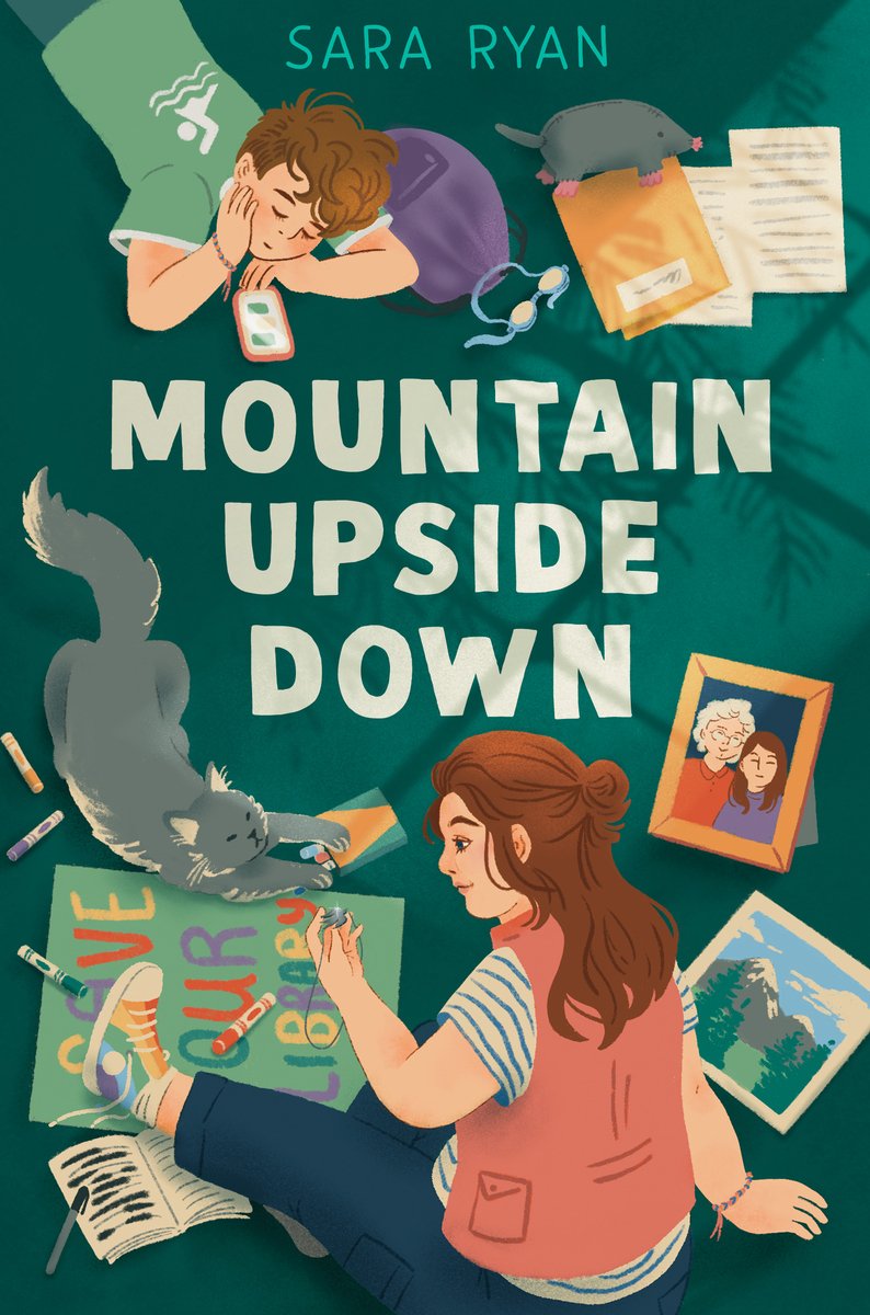 Book cover of Mountain Upside Down by Sara Ryan, featuring two light-skinned youths - one with long, straight brown and and the other with short, curly brown hair - sitting on a floor cluttered with various items, such as pictures, manila folders, and a sign that reads "Save Our Library."
