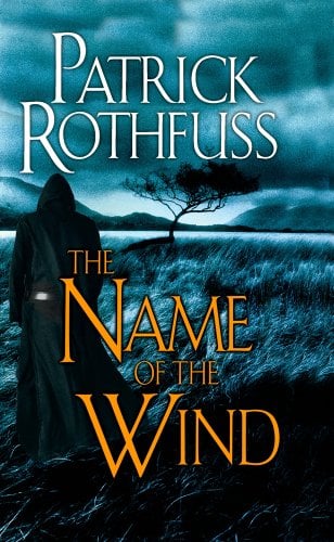The cover of The Name of the Wind by Patrick Rothfuss. A black cloaked figure looks out across a windy grassy plain, water and mountains in the background. The sky is cloudy above. The whole image has a blue tint.