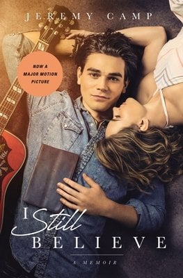 I Still Believe book cover modeled after the movie by the same name. Features a man and a women laying on the ground, the man wearing a blue denim shirt and holding a bible while a red guitar lies next to him. The woman is wearing a sundress.