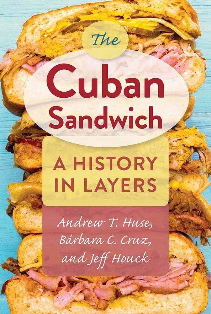 Cover of The Cuban Sandwich: A History in Layers by Andrew T. Huse. Four Cuban sandwiches are stacked together to show the inner ingredients. The wall behind is light blue.