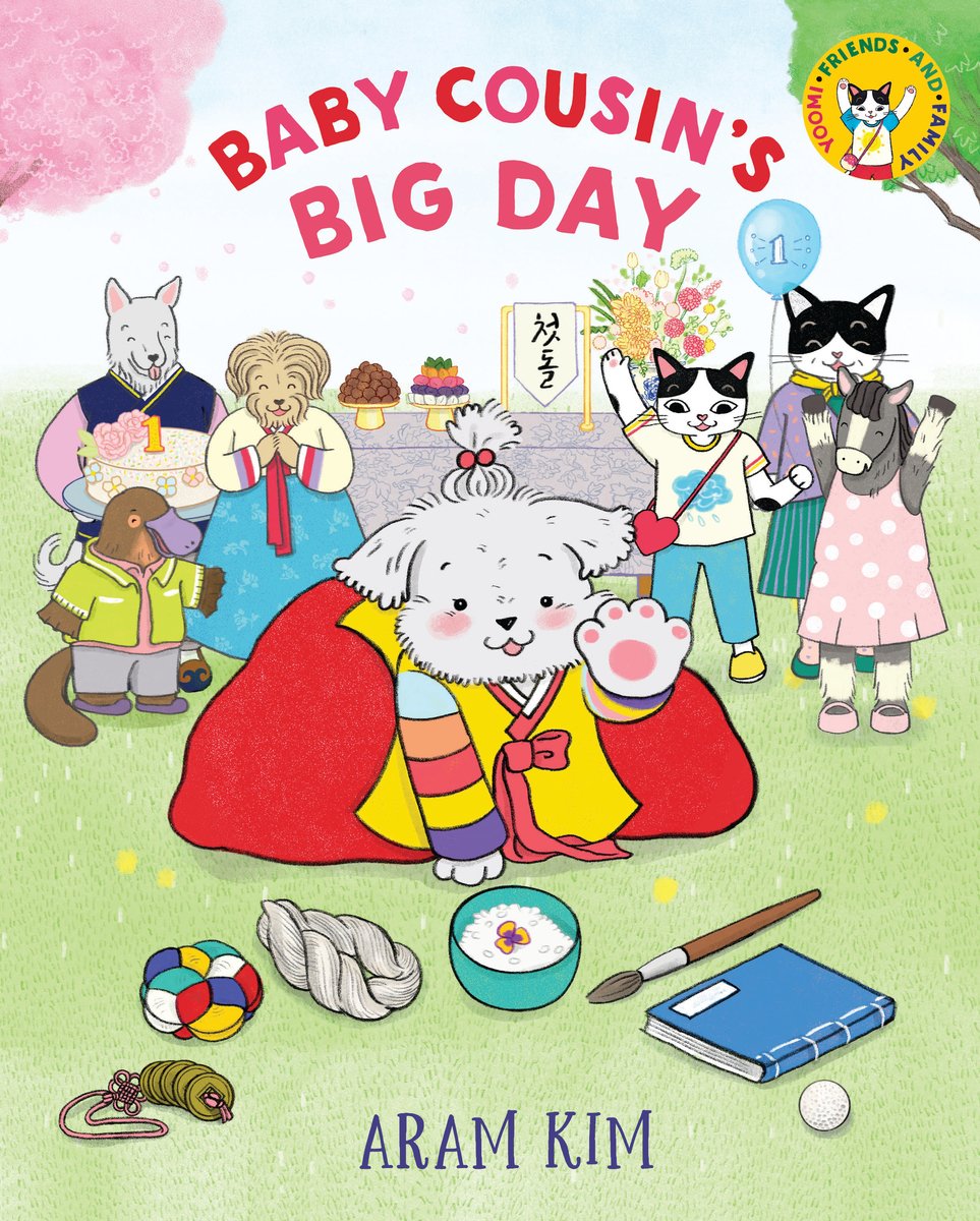 Book cover of Baby Cousin's Big Day by Aram Kim, featuring a white humanoid puppy wearing a yellow and red hanbok reaching out towards several objects on the ground, including a paintbrush, a book, a bowl of rice, and a string of coins. Several more humanoid animals cheer in the background.