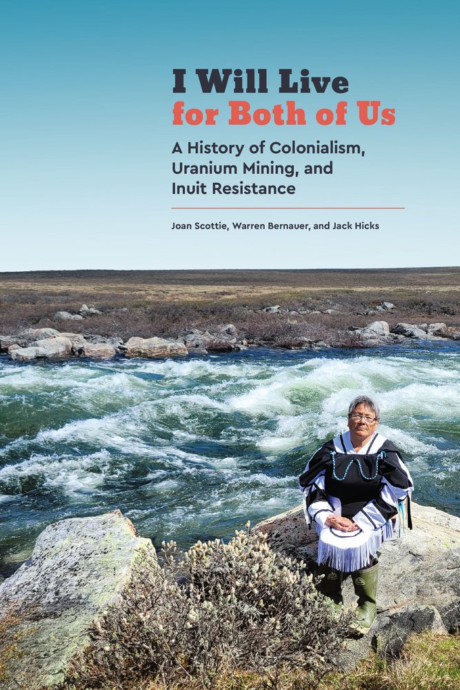 I Will Live for Both of Us by Joan Scottie, Jack Hicks, and Warren Bernauer depicting an Inuit woman standing on a rocky shore in front of whitewater river. She is looking at the photographer with her hands folded in front of her.
