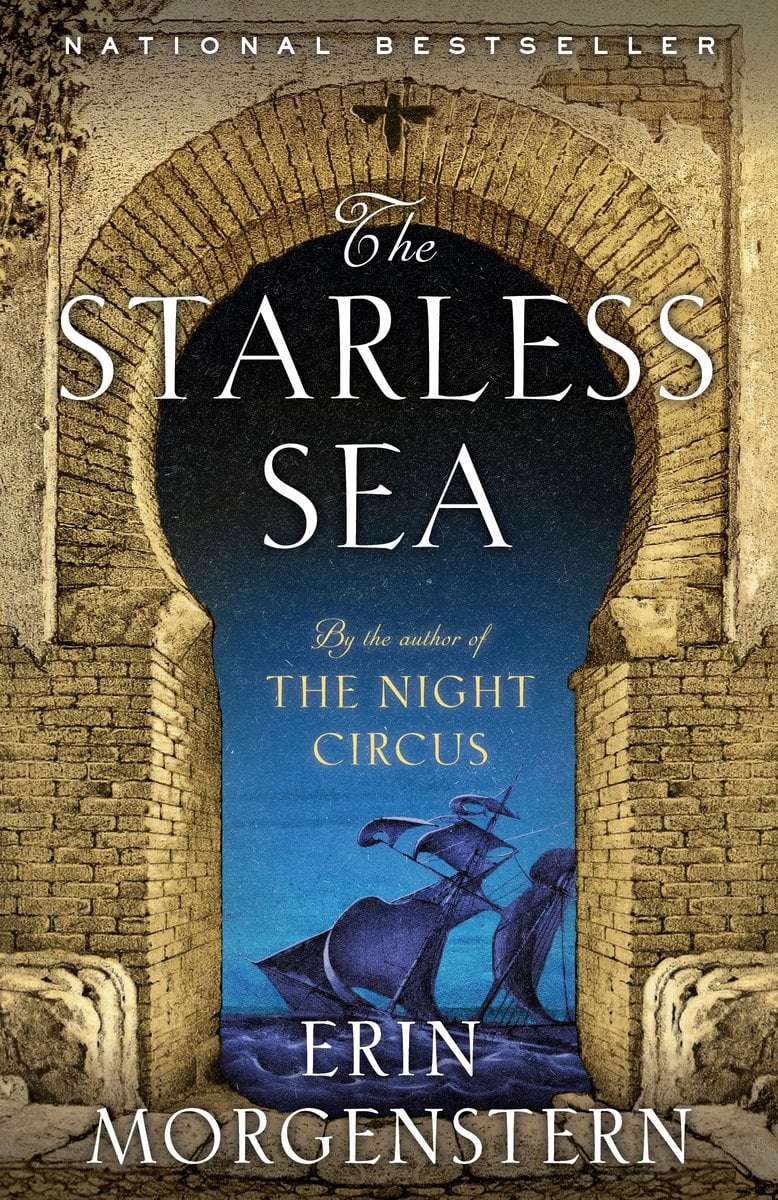 The book cover for The Starless Sea by Erin Morgenstern. A golden bricked archway opens out to a dark purple ship against a medium blue sky. The title is over the top in white text.