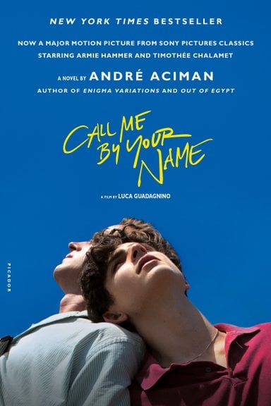 Call Me By Your Name by André Aciman book cover. Two young men are depicted from the chest up as they look up at a bright blue sky. The man on the right has dark hair and is wearing a red shirt as he rests his head on the other's shoulder. The other man is obscured by the first but wears a light washed denim button down and is leaning into the other.