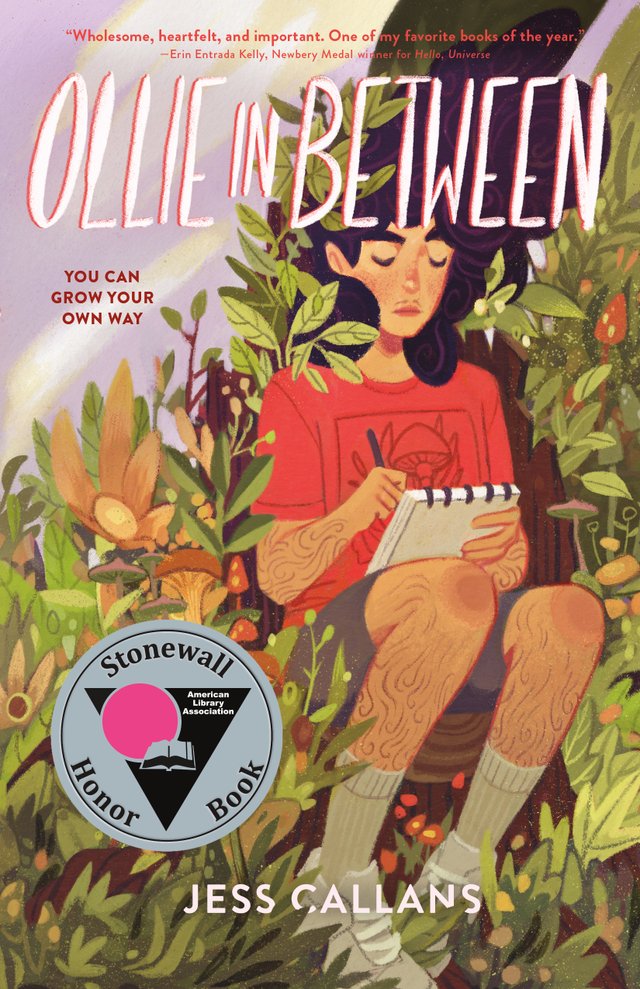 Ollie In Between by Jess Callans, book cover. A person with long black hair in curls, a red shirt, and gray shorts is holding a notebook and writing in it, sitting on a log with leaves and bushes surrounding them.