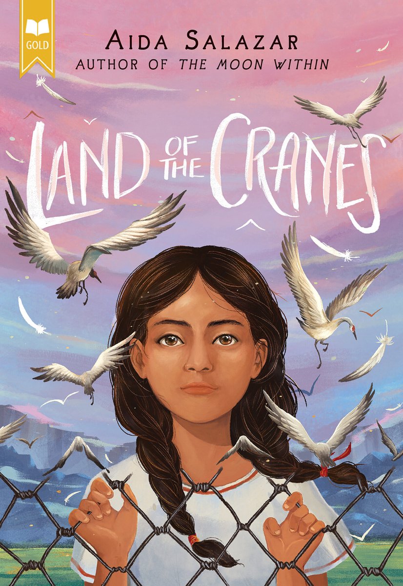 Cover of Land of the Cranes by Aida Salazar. A brown skinned girl with dark hair in braids holds onto a chain linked fence. White cranes fly around her. In the background is a pink and blue sky against mountains.