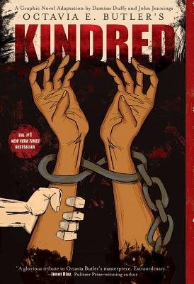 The cover of Kindred: A Graphic Novel by Octavia E. Butler, adapted by Damian Duffy, illustrated by John Jennings. The graphic novel adaptation of the original novel features two raised Black arms chained with a white hand grasping the left forearm against a dark black and red background.