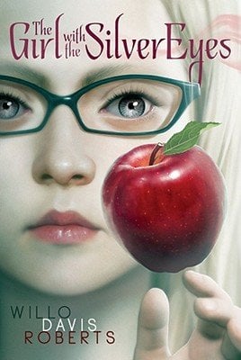 The Girl With the Silver Eyes by Willo Davis Roberts middle-grade book cover depicting an up-close young blond haired girl with silver eyes and green glasses. In front of her cheek floats a bright red apple with her hand visible slightly beneath it.