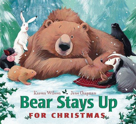 Book cover of "Bear Stays Up for Christmas," written by Karma Wilson and illustrated by Jane Chapman, featuring an illustration of a large brown bear surrounded by various woodland animals, laying in a snowy forest.