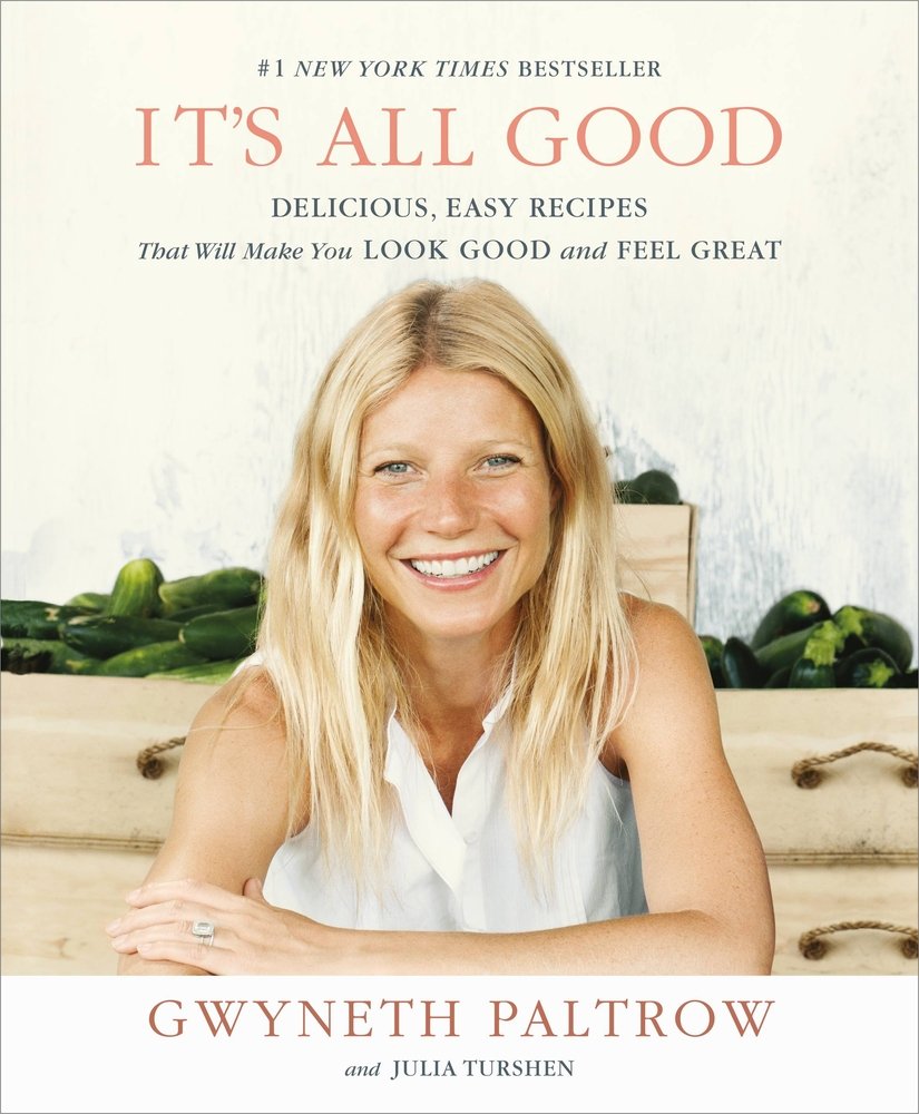 It's All Good: Delicious, Easy Recipes That Will Make You Look Good and Feel Great by Gwyneth Paltrow, book cover. A blonde haired young woman smiles into the camera while leaning on a surface. Behind her, zucchini sits on light brown countertops with brown drawers beneath.