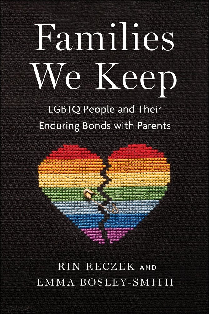 The background is black and holds an embroidered broken heart made in rainbow stripes with a safety pin trying to keep it together.