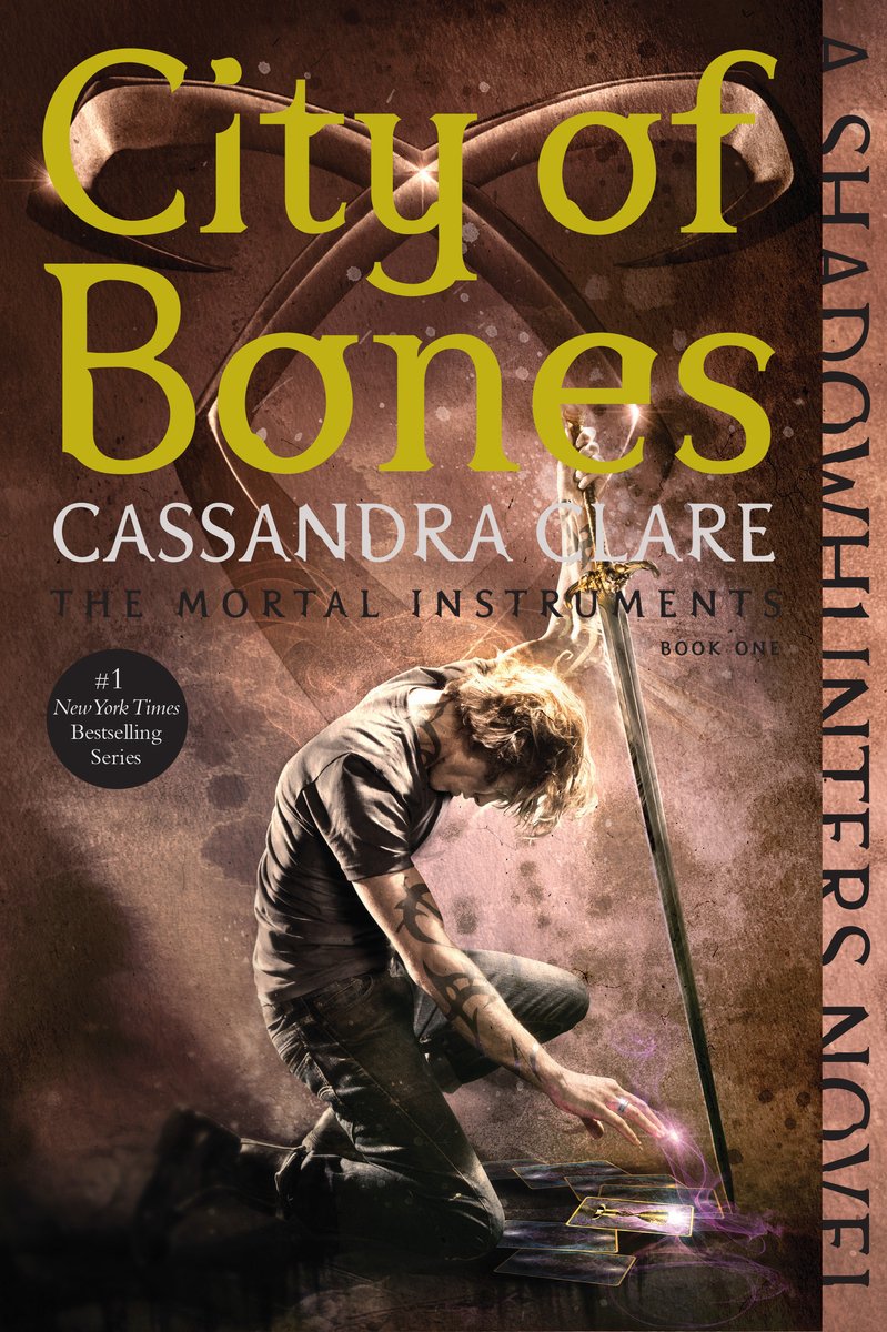 The cover of CIty of Bones, the first book in a YA urban fantasy novel, depicts a young blond man with black tattoos kneeling with his right hand reaching down to touch of cards on the ground as his left hand holds a sword with the blade tip to the ground against a bronze background