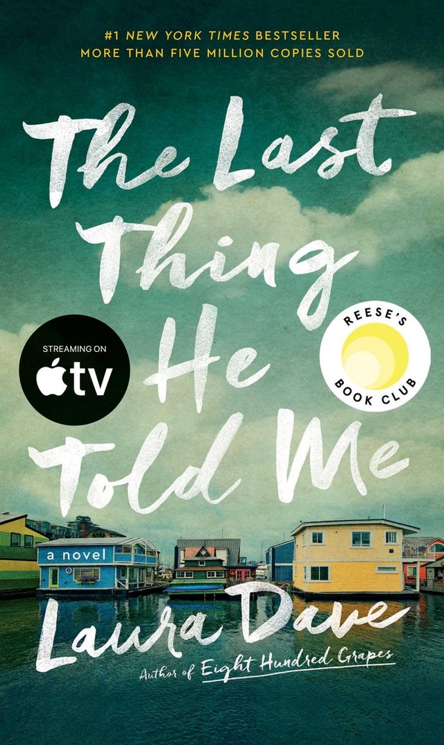 Cover of The Last Thing He Told Me by Laura Dave. Three different multicolor building sit on the edge of a lake. The sky is cloudy and dark.