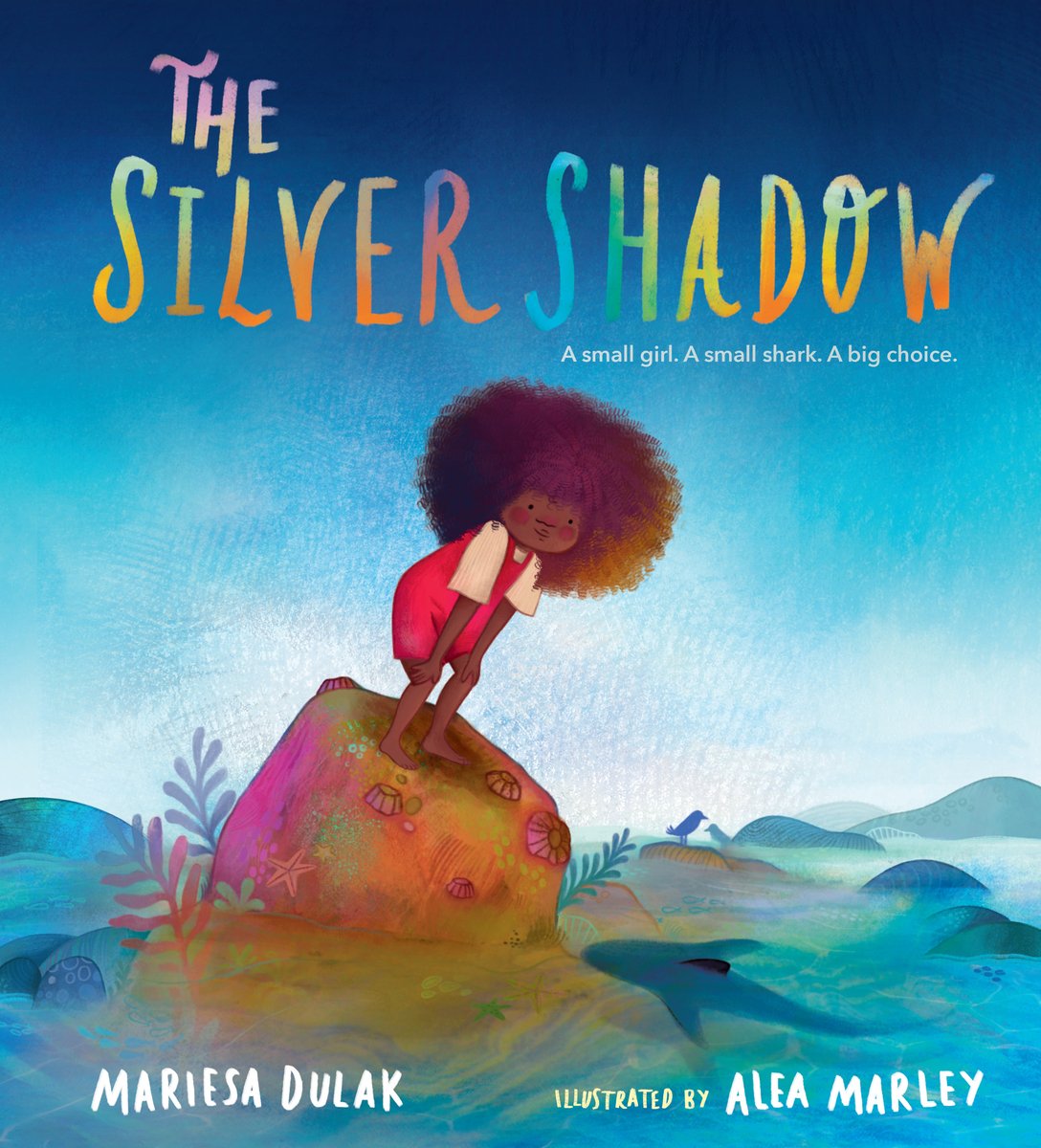 Book cover of The Silver Shadow by Mariesa Dulak, Illustrated by Alea Marley, featuring a brown-skinned girl with a large brown afro standing on an ocean rock and gazing into a tidepool, where the silhouette of a small shark can be seen swimming.