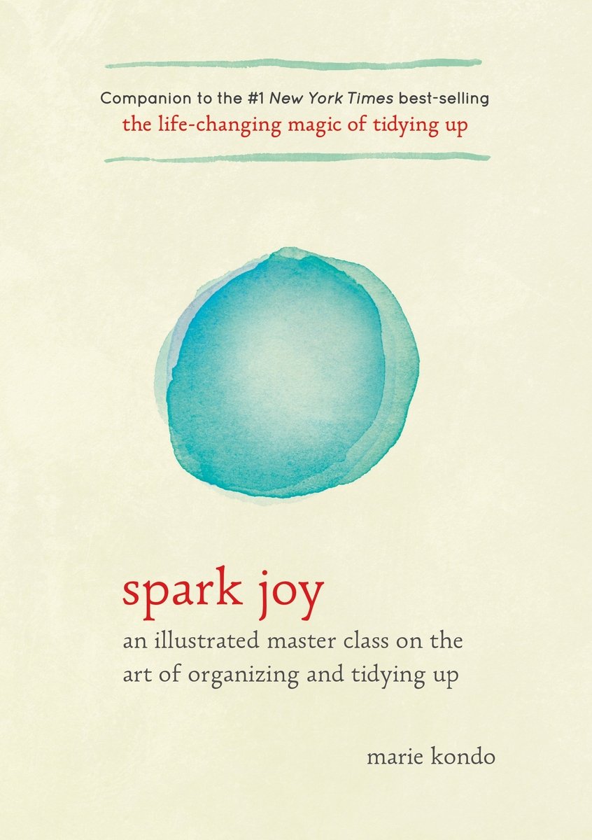 The background is a pale yellow with two translucent blue circles, one on top of the other. Marie Kondo's number one New York Times' best-selling status is at the top of the cover, and the title of the book, Spark Joy, is in red above "an illustrated master class on the art of organizing and tidying up" and Marie Kondo's name in all black, lower-case lettering.