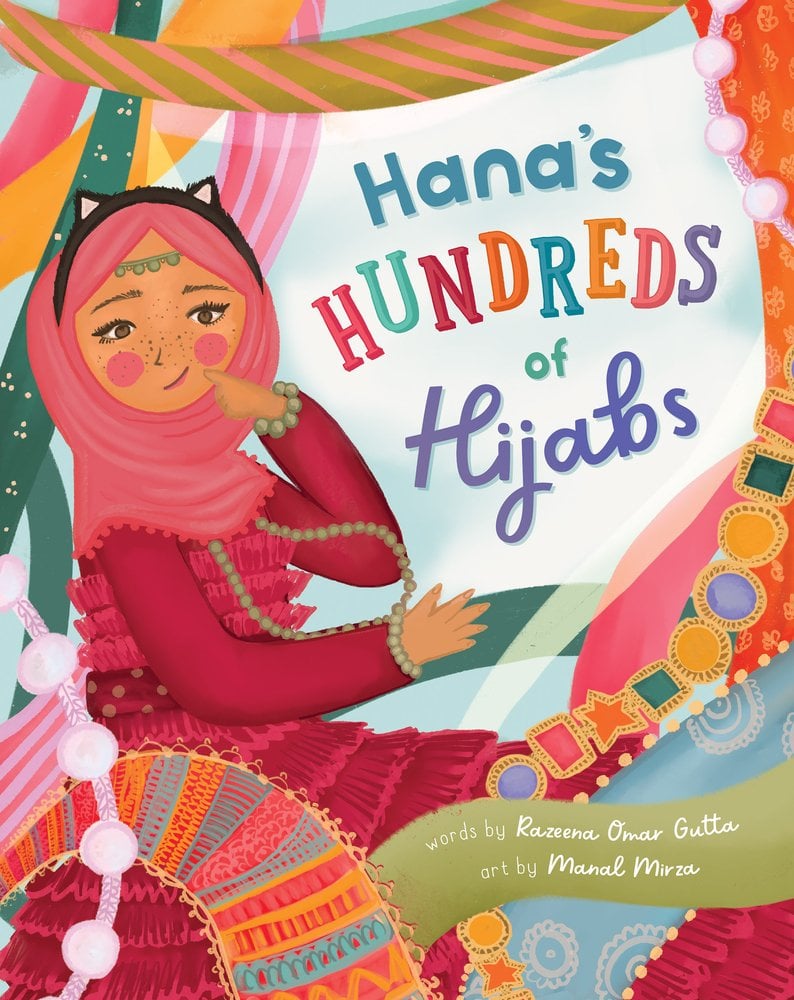 The book cover of Hana’s Hundreds of Hijabs by Razeena Omar Gutta, Illustrated by Manal Mirza, features a smiling brown-skinned girl wearing a pink hijab with black cat ears over it; she is surrounded by swathes of colorful fabric and strings of beads.