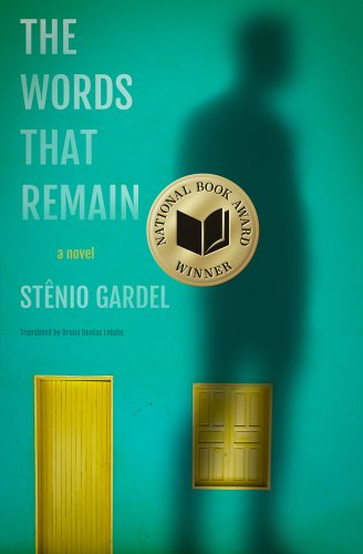 Translated Literature: The Words That Remain by Stênio Gardel, translated by Bruna Danatas Lobato, book cover. An aqua house with a yellow wooden door and window sheds. A large shadow of a male figure hovers over the house and the window facing the right.