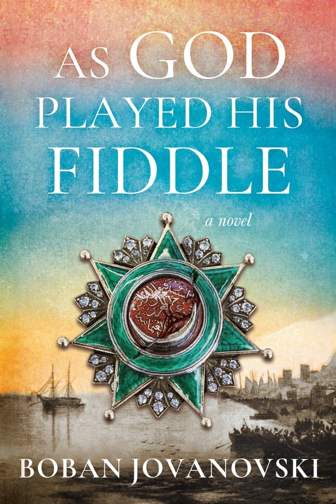 As God Played His Fiddle by Boban Jovanovski book cover features a background of a watercolor sunset made of blues, yellows, and oranges with a harbor at the bottom. The harbor has a boat out in the water and the skyline of a city can be seen in the background. The title is in all caps, white sans serif font with a nautical red and emerald green symbol in center-bottom. The author's name is at the very bottom in all caps.