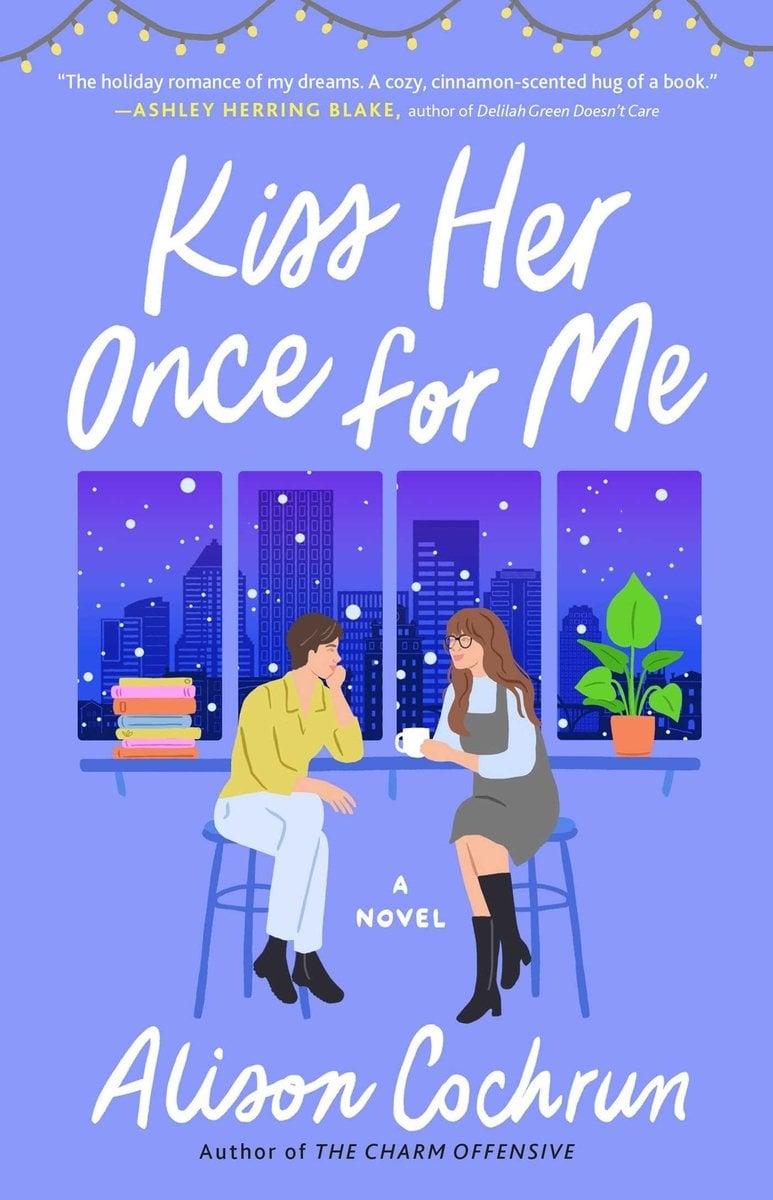 Kiss Her Once for Me by Alison Cochrun, a romance book cover depicting a girl with a gray dress sitting across from a girl with a yellow shirt. They are both seated in front of a window depicting a city view of assorted buildings. The title is printed in a cursive white font.