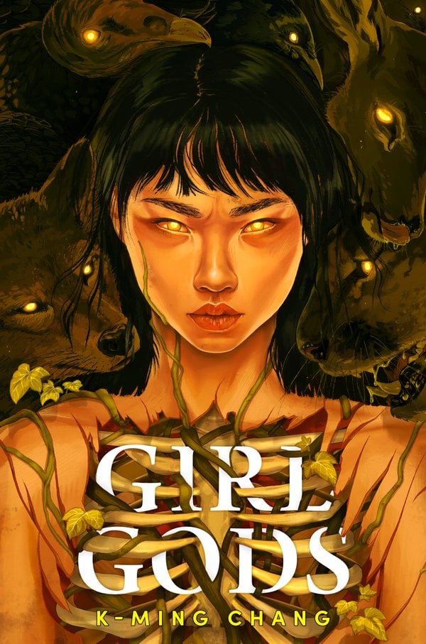 Girl Gods by K-Ming Chang is a YA fantasy novel featuring a portrait of a young girl at the center, facing the reader. She has tan skin, black hair with choppy bangs, and glowing yellow eyes. Above her shoulder, there are three gray wolves. Leafy vines travel around her neck and her rib cage is open, baring her skeleton. The title is written in white text, spliced between her bones.